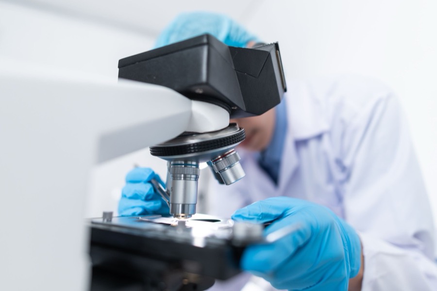 Pesquisador de jaleco branco operando microscópio em laboratório